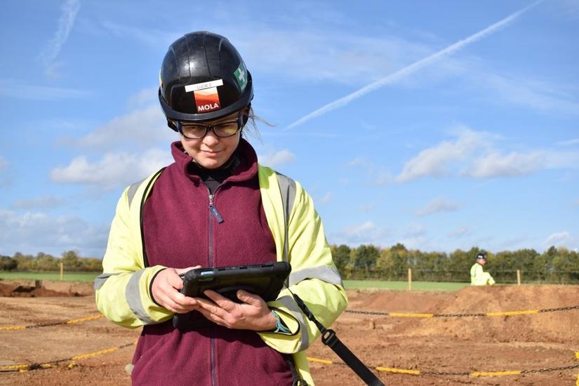 An archaeologist in high-vis using a tablet