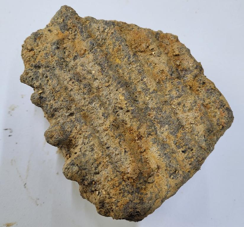 A piece of dark millstone with long grooved lines on its surface